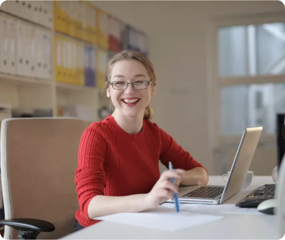 Woman using a laptop and writing notes at a desk in an office