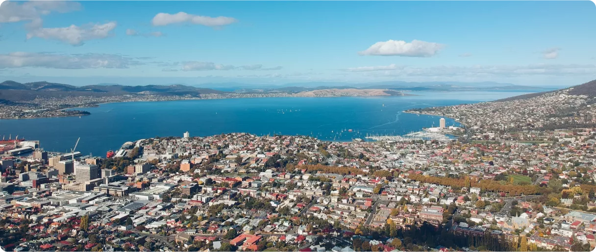 Aerial view of a coastal city with colorful buildings, a blue bay, and distant mountains under a clear sky