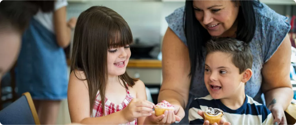 A woman and two children are smiling and holding decorated cupcakes in a kitchen setting