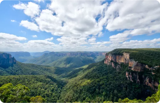 A panoramic view of lush green mountains and cliffs under a partly cloudy sky