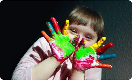 Child smiling and showing hands covered in colorful paint