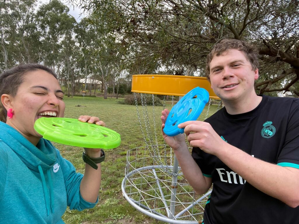 A man and a woman holding frisbees. The woman is jokingly biting her frisbee.