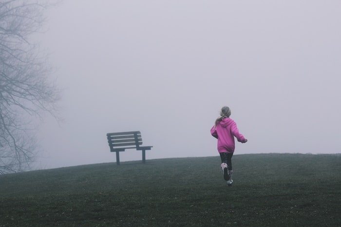 A girl in a foggy park running away from the camera.