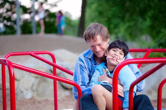 Father holding disabled son on merry go round at playground