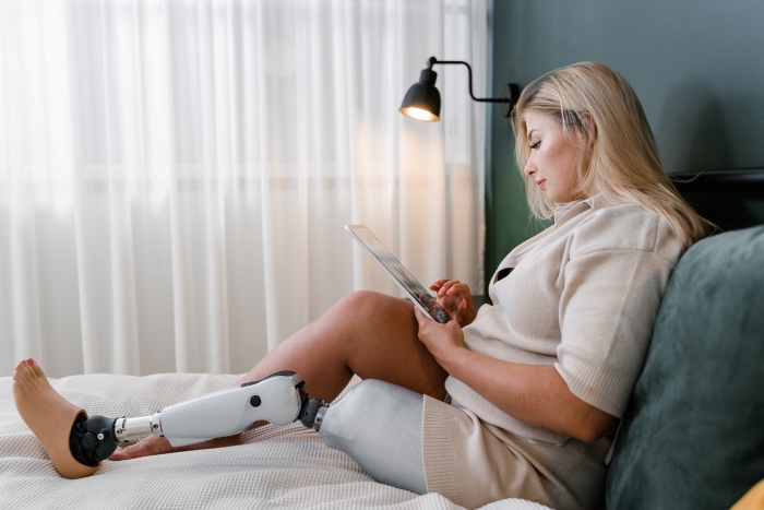 A woman with a prosthetic leg relaxes on a bed whilst scrolling her iPad.