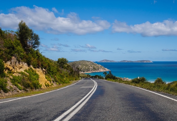 An open coastal road with views of the ocean and some small islands off in the distance.