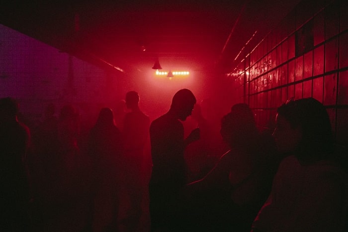 A dark hazy red light filled nightclub filled with people.