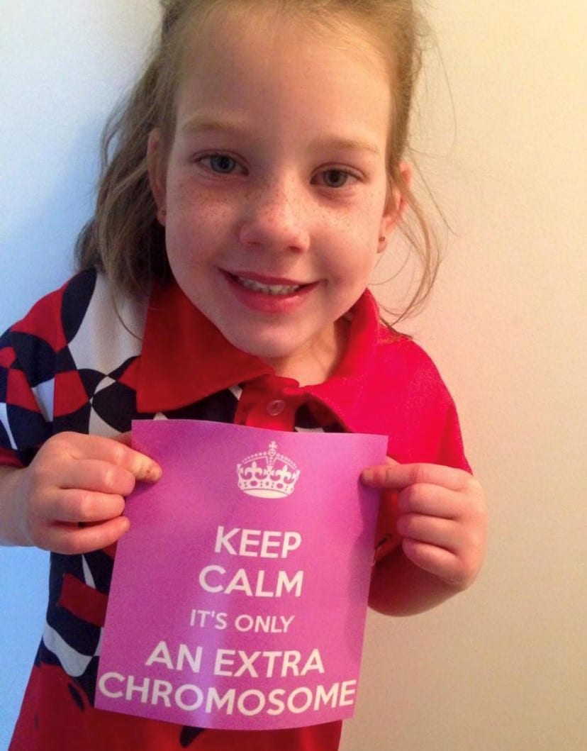 Close up of a young girl holding a pink sign which reads 'Keep calm: it's only an extra chromosome.'