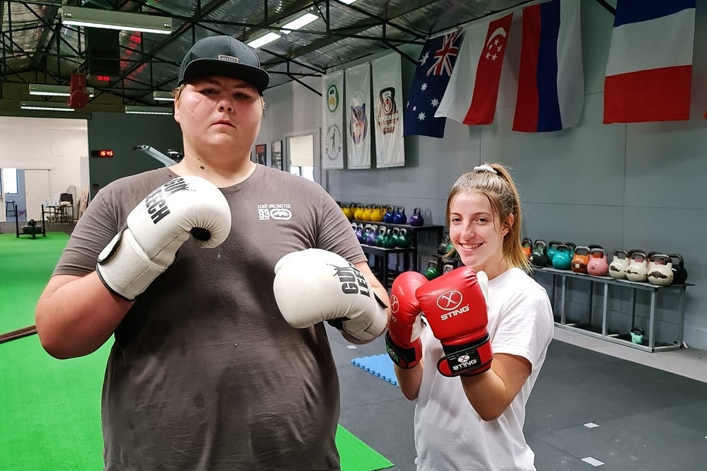 A habit coach (right) and a client (left) in a training facility wearing boxing gloves