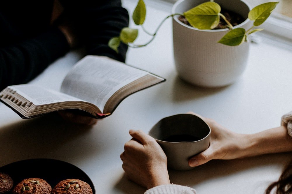 Two people sitting at a table holding a book and a drink