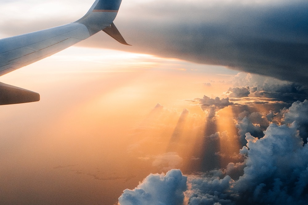The wing of a plane flying over clouds in orange sunlight 
