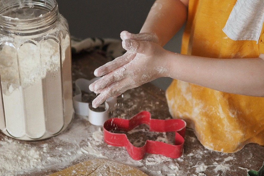 A close-up of a child with flour and gingerbread men-shaped cookie-cutters