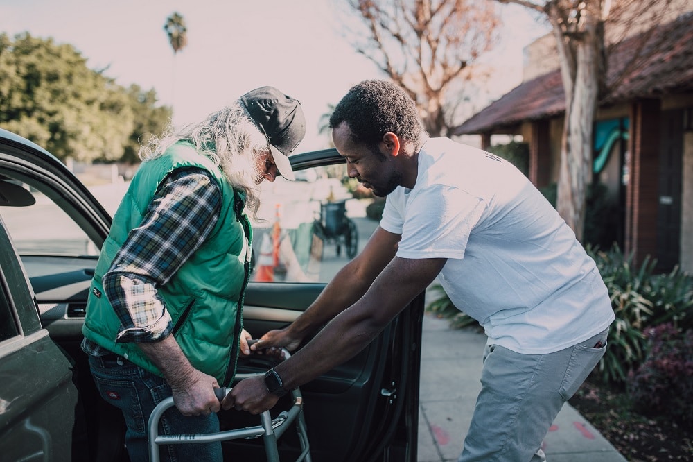 A carer helping a person with a walker get out of a car. 