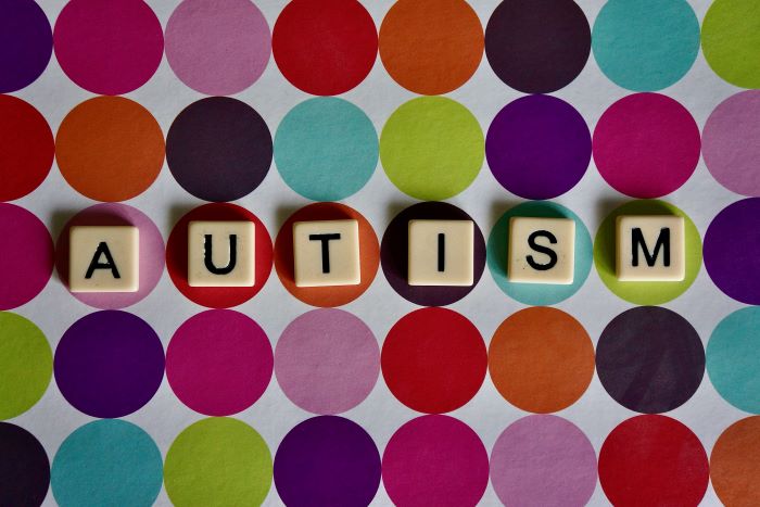 Tiles from the game Scrabble spell out 'autism' over a multicoloured background.