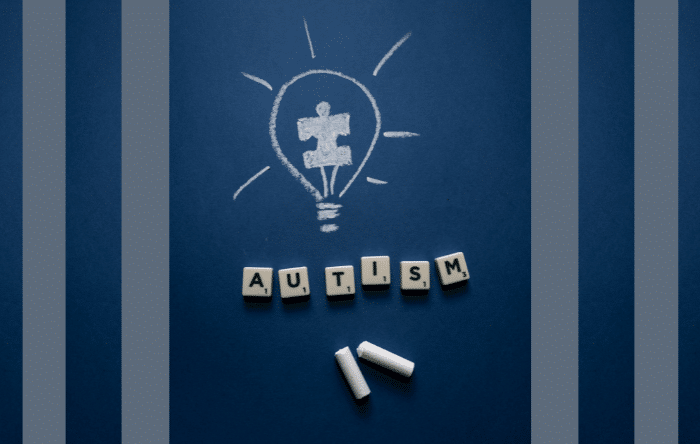 A chalk drawing of a puzzle piece inside a lightbulb with 'autism' spelled out underneath in Scrabble tiles.