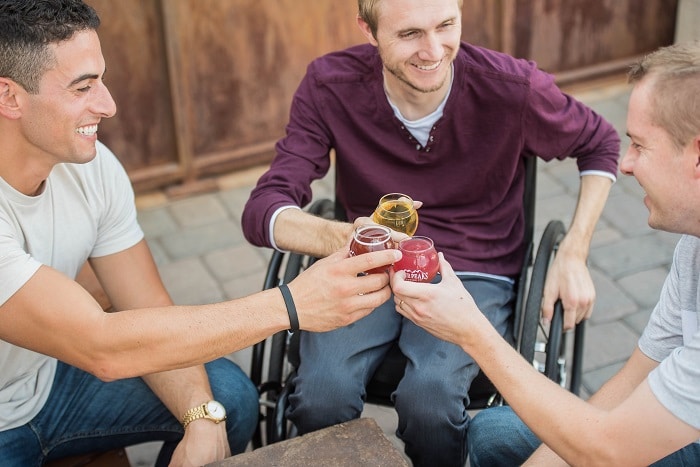 A man in a wheelchair and his friends toast their drinks together in the air.