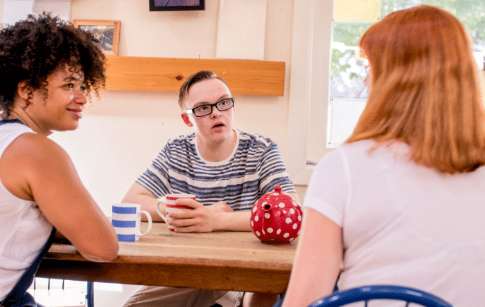 A young man with down syndrome converses with two friends at a table.