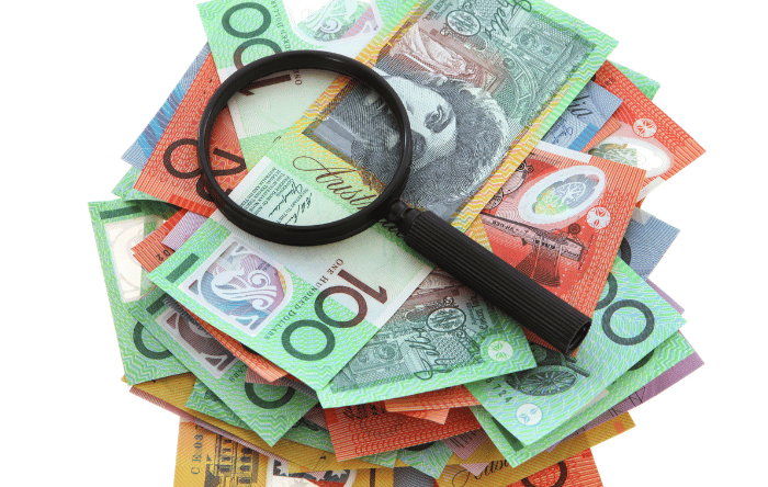 A black magnifying glass sits on a pile of Australian money.