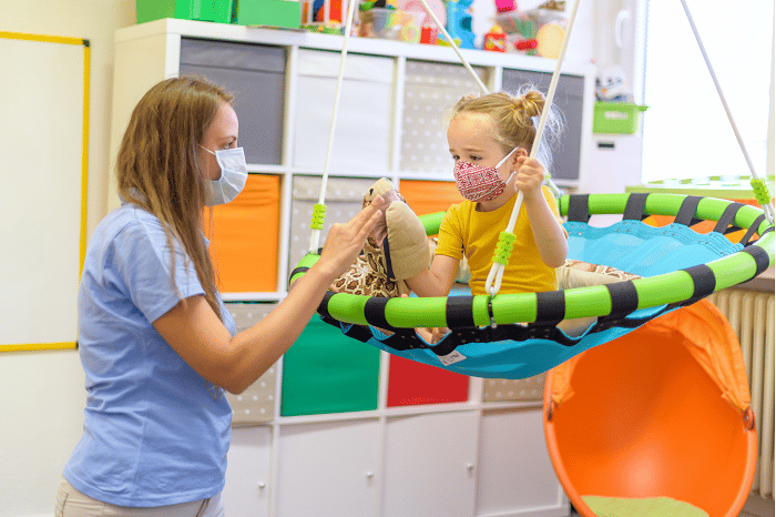 A woman playing with a child on an indoor swing. They are both wearing face masks.