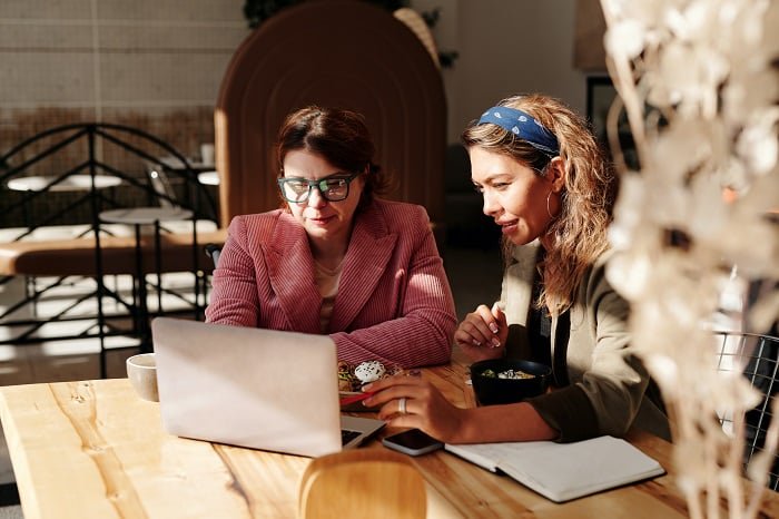 Two women sitting at a cafe, working on a laptop.