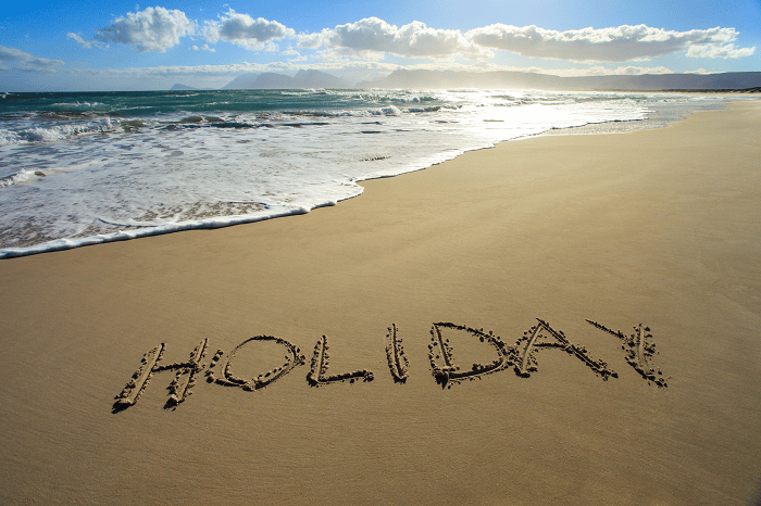 The word 'HOLIDAY' written in the golden sand of a pristine beach.