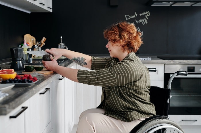 A woman in a wheelchair cutting fruit in a kitchen.