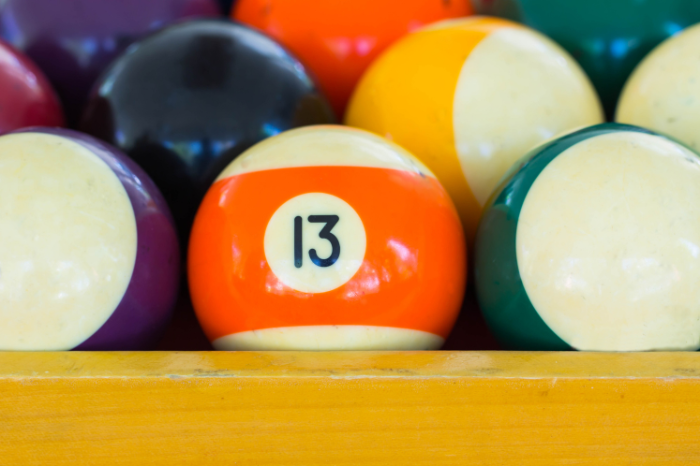 An orange number thirteen pool ball amongst other pool balls.