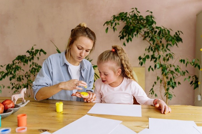 A mother and young hand painting on a table.