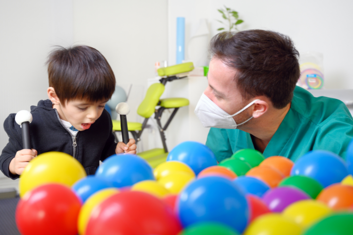 A man wearing a mask, talking to a child. Colourful plastic balls can be seen in the foreground.