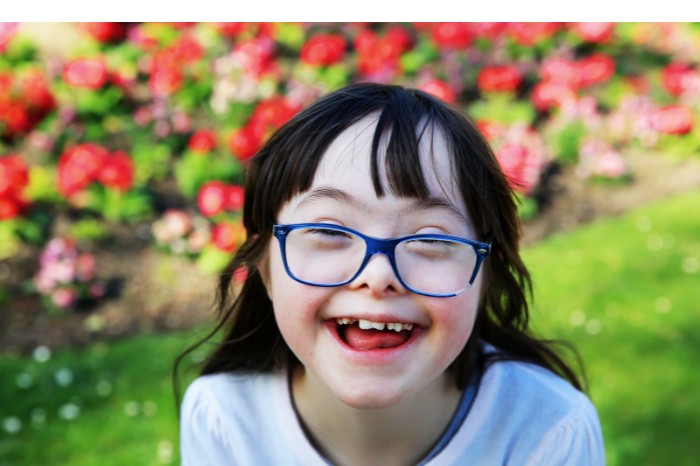 A young girl in a garden smiles at the camera.