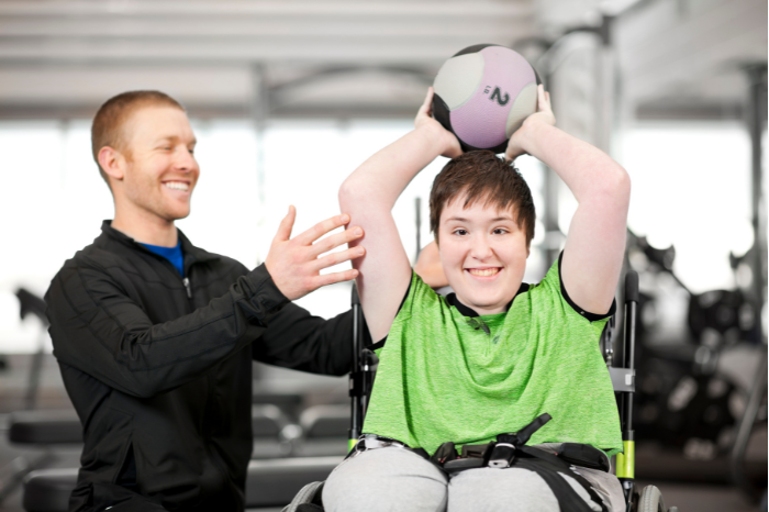 A woman in a wheelchair holds a ball above her head and a man stands alongside her.