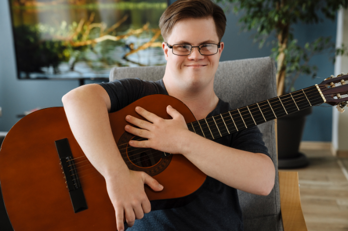 A young man with Down Syndrome holds a guitar.