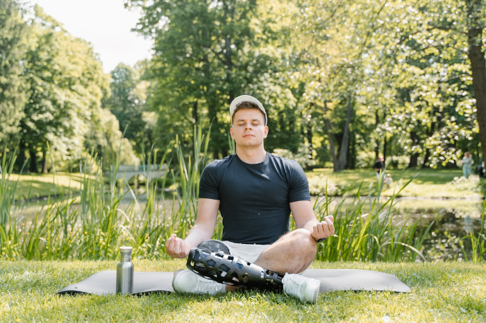 A young man wearing activewear and prosthetic leg meditates in a park.