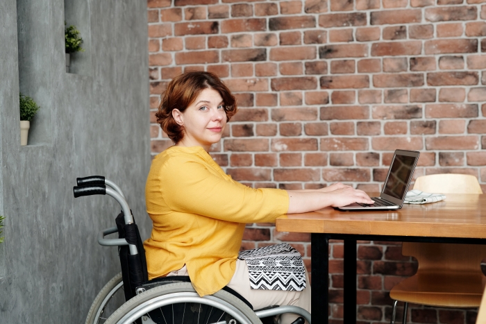 A woman sits in her wheelchair at a table doing work on her laptop.