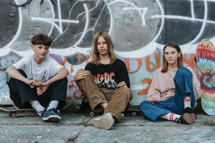Three teenagers sit in front of a graffiti art wall.