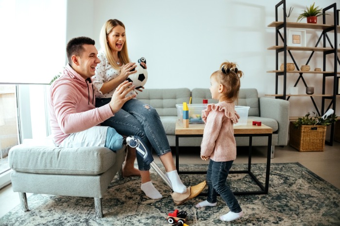 A father with a prosthetic leg enjoys time with his wife and child in their lounge room.