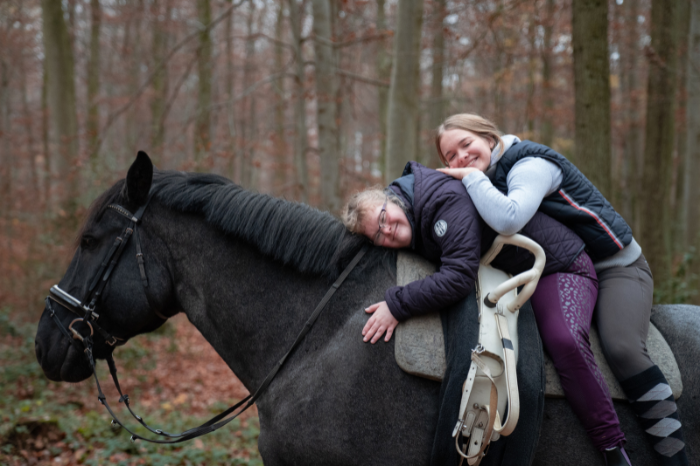 Two smiling people sit on the back of a black horse.