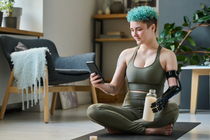 An athletic young woman with curly blue hair and a prosthetic arm checks her mobile phone.
