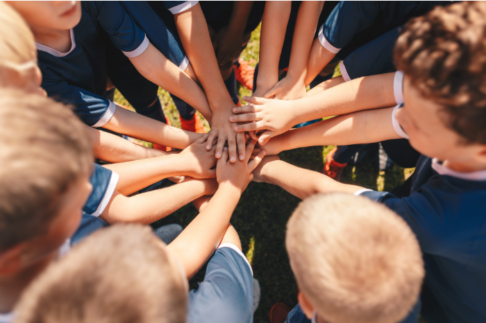 A sports team of young children put their hands together at the centre of their huddle.