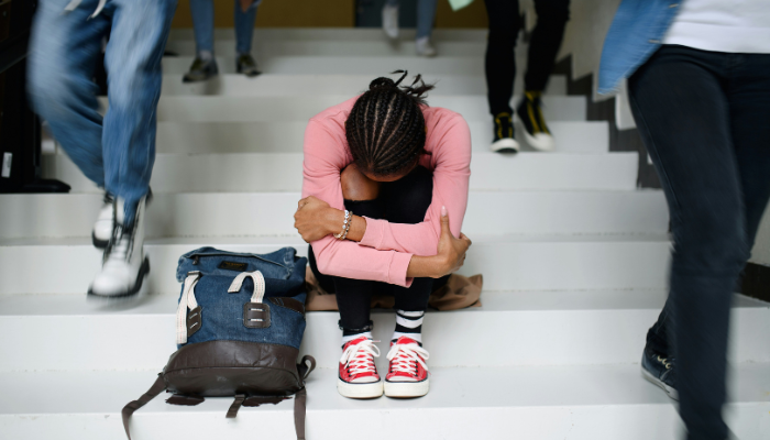 A person sitting on stairs hugging their knees in a public setting.